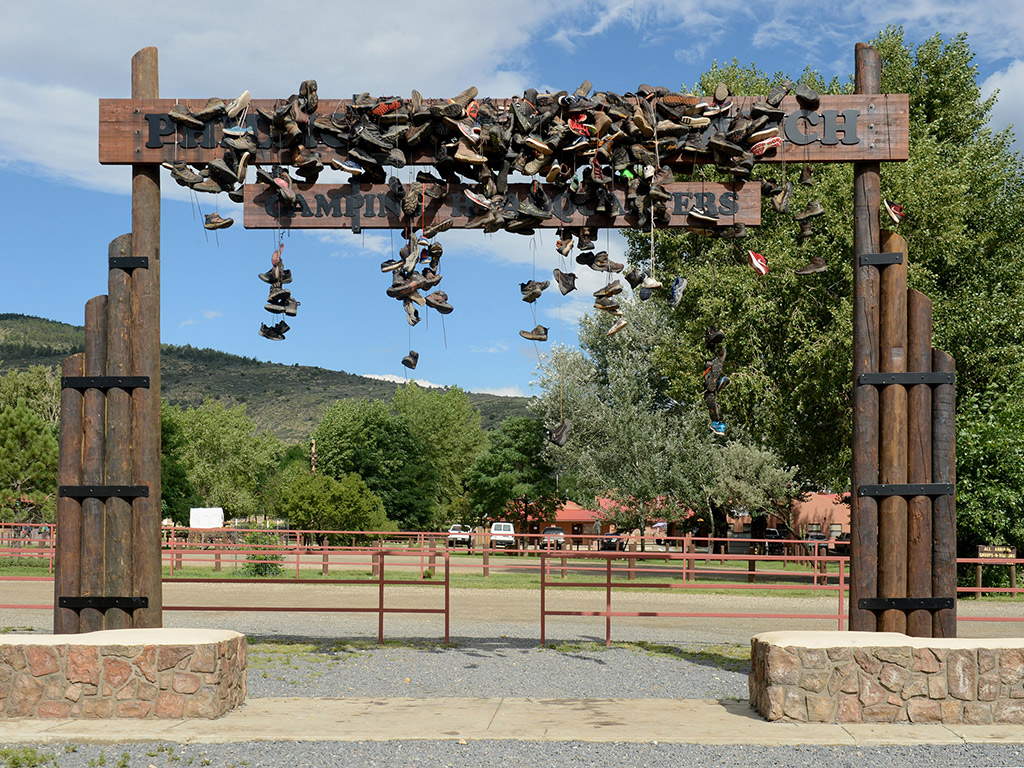 A large wooden entrance sign covered in hiking shoes that have been thrown over the sign and tied by shoe laces